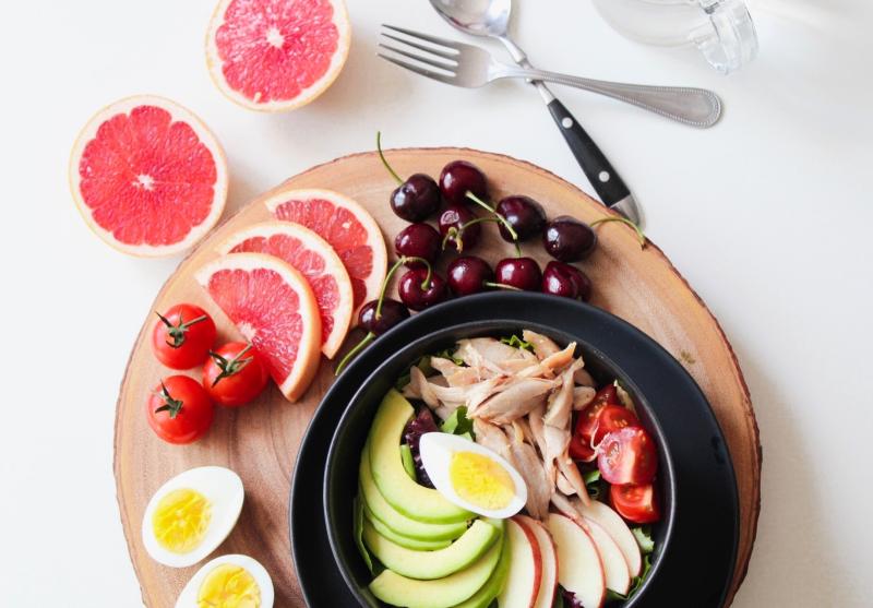 Healthful items including grapefruit, avocado, hard-boiled egg, and more on a plate with fork and spoon