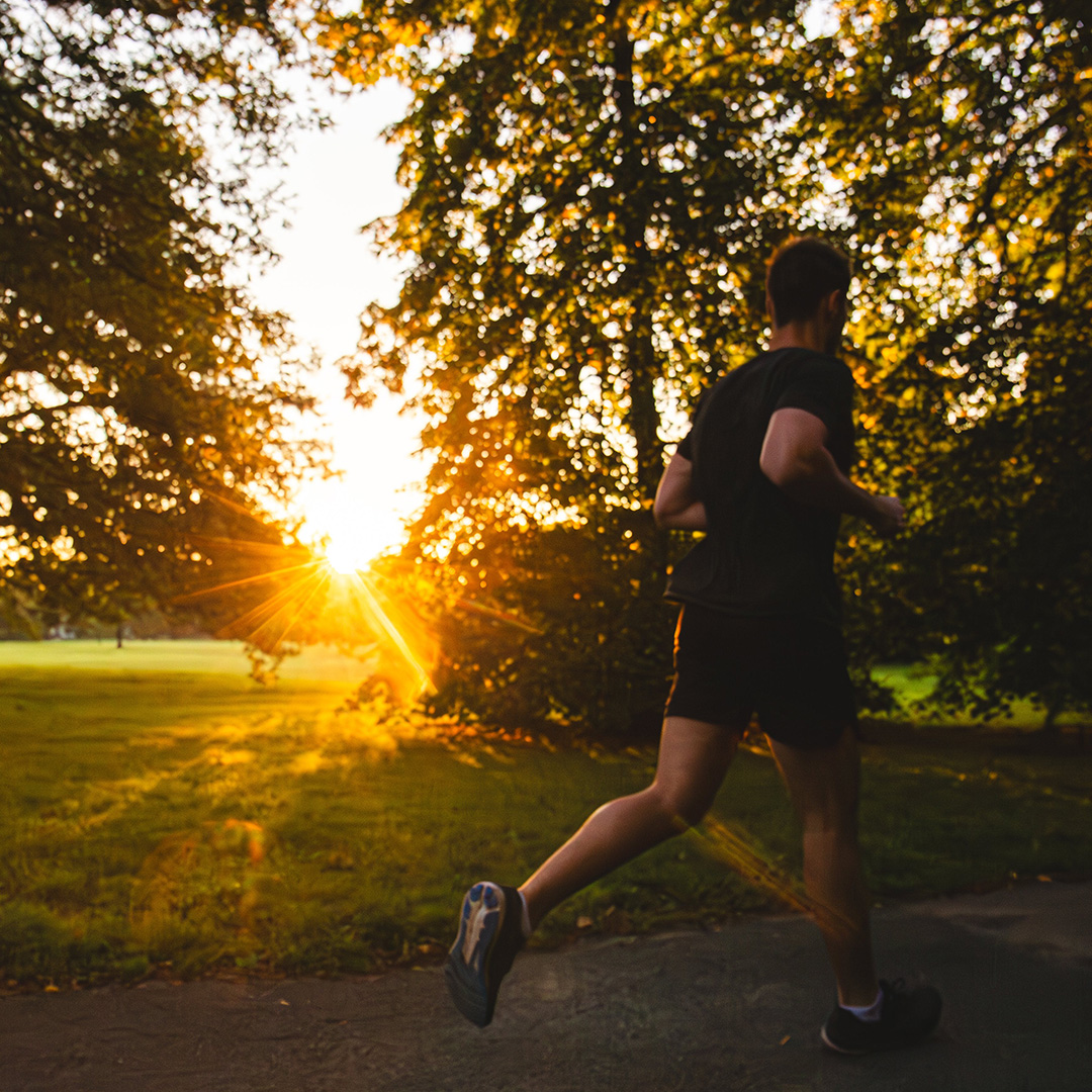 Runner on a path in a park with the sun setting in the background.
