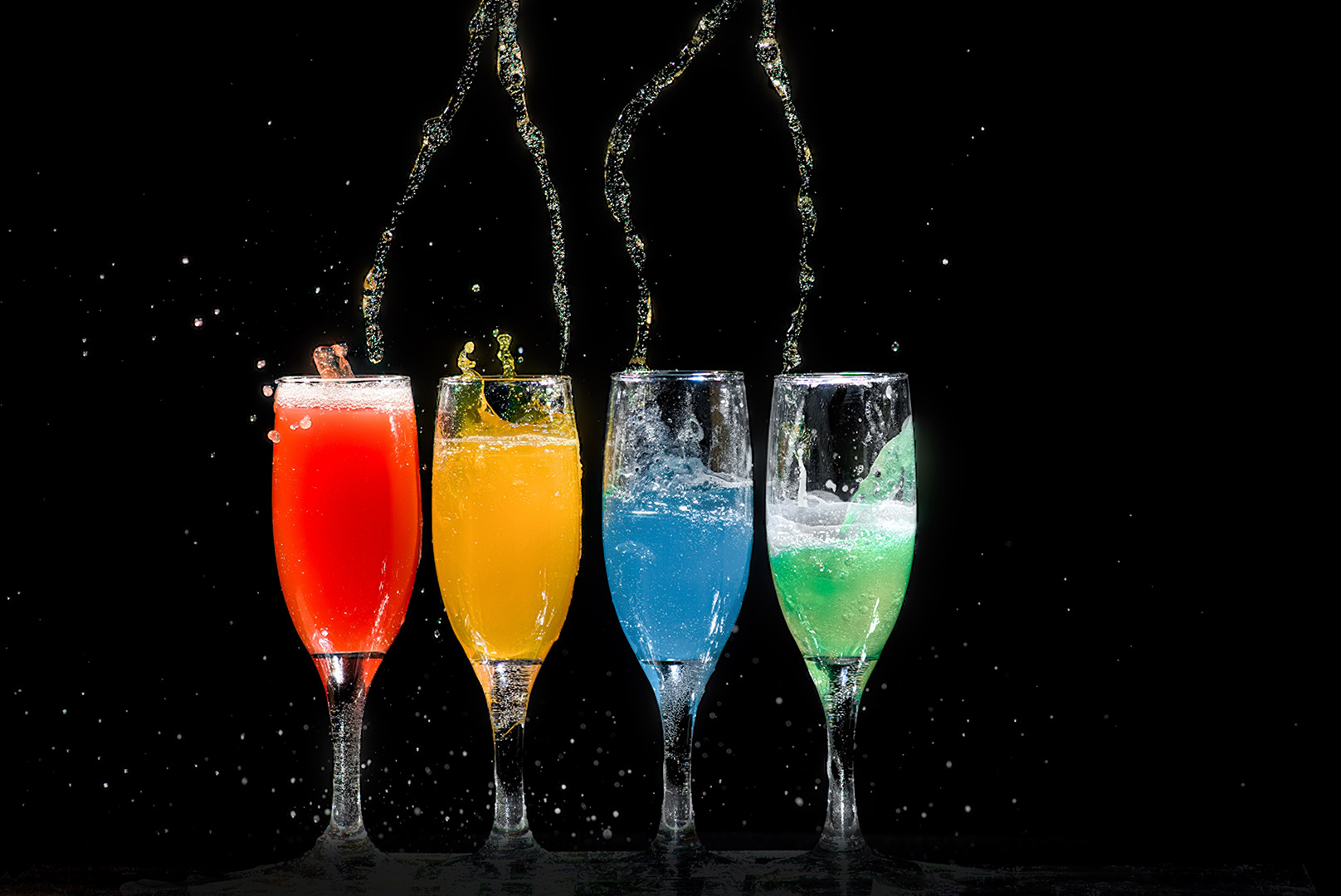 Long stem alcohol glasses sit in front of a black background with bright colored drinks inside