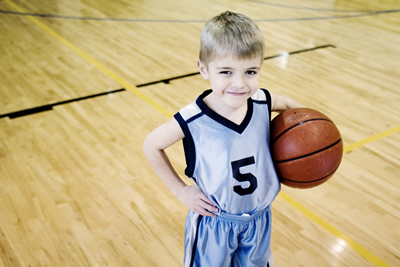 Child holds a basketball under their arm on a basketball court