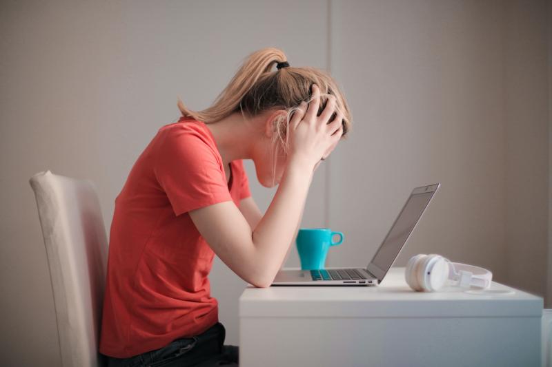 Individual with hand on her head in stress looking at a computer