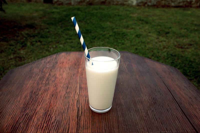Glass of milk with a blue swirl straw on a wood table with grass in the background