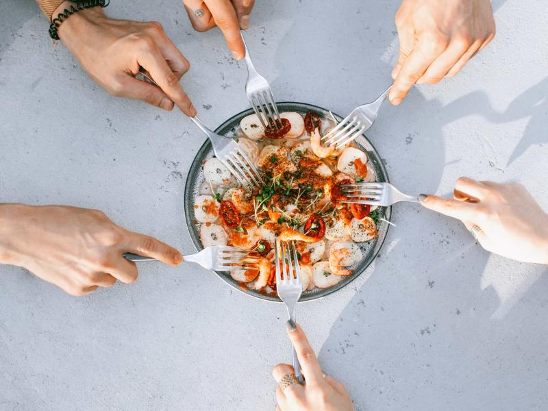 Multiple hands with forks reach for food at the center of the table