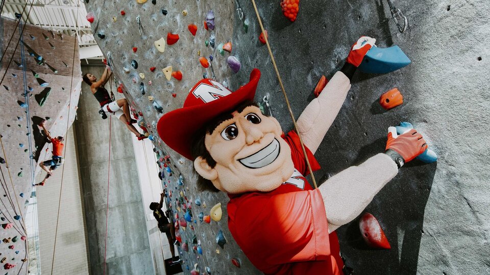 Herbie Husker climbs the climbing wall in the Outdoor Adventures Center