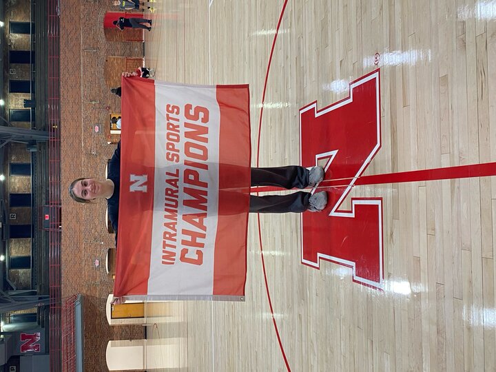 Person holding a red and white "Intramural Sports Champions" banner on a gymnasium floor.