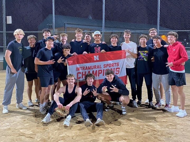 Group of students posing with flag on softball infield dirt.