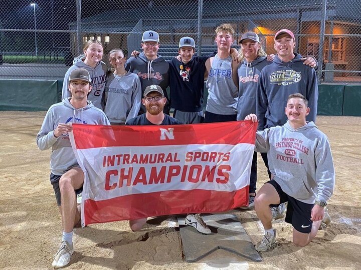 Group of student posing with flag on softball infield dirt.