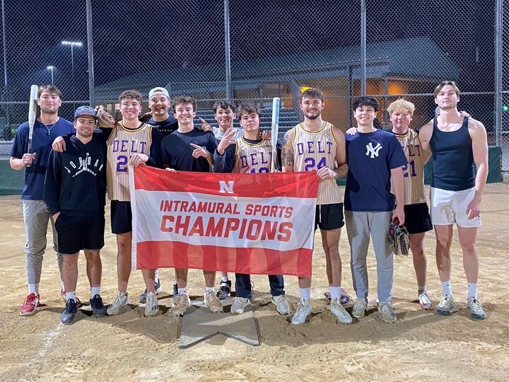 Group of students posing with flag on softball infield dirt.