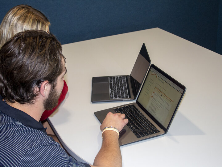 Two people sitting at a table, working on laptops in a modern, blue-walled room.
