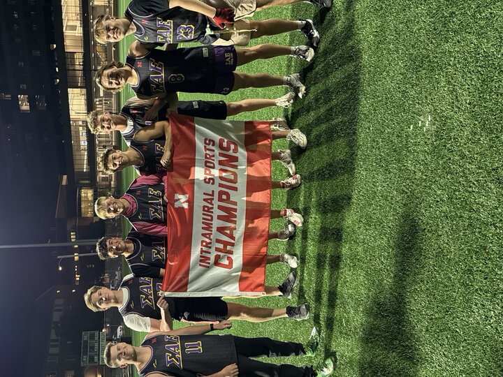 Seven individuals holding a red banner reading "Intramural Sports Champions" on a green field at night.