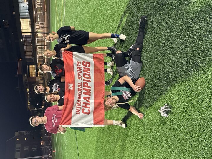 Group of players on a sports field holding a "Intramural Sports Champions" banner at night.