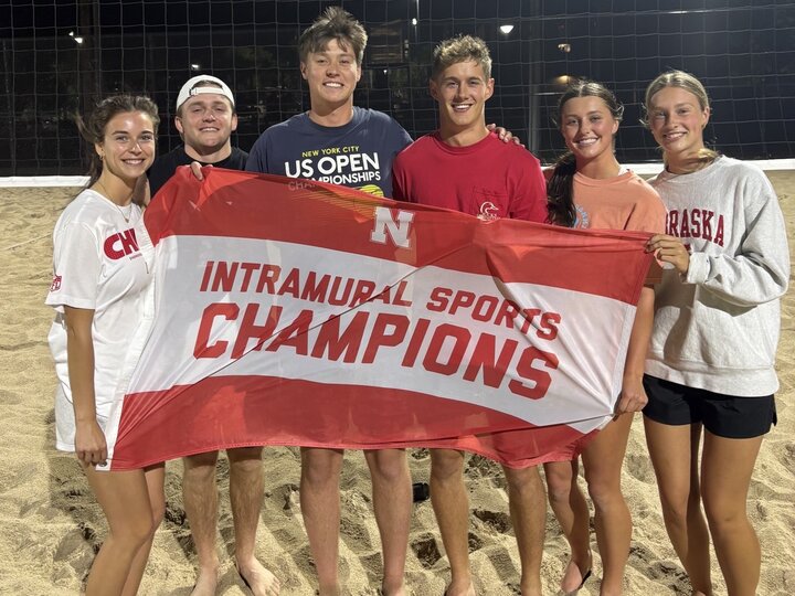 Group of students posing with flag at sand courts.