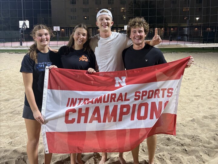 Group of students posing with flag at sand courts.