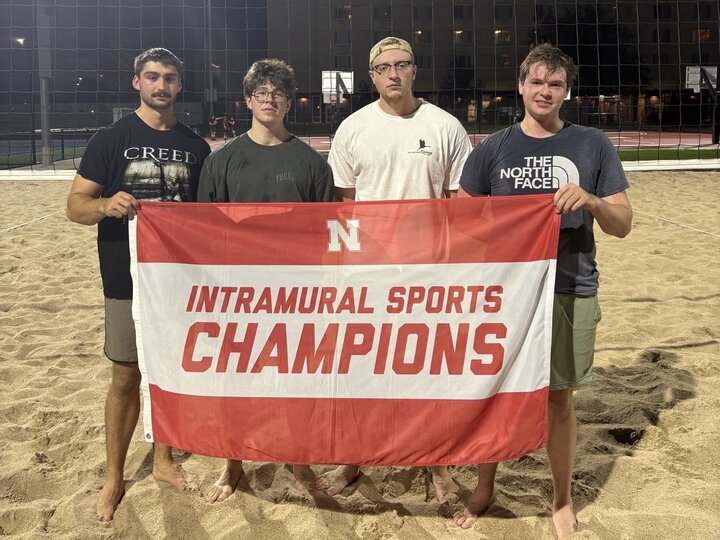 Group of students posing with flag at sand courts.