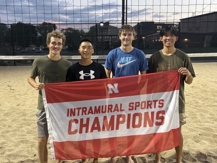 Group of students posing with flag at sand courts.