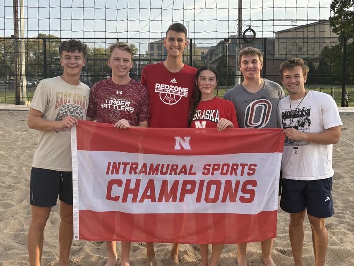 Group of students posing with flag at sand courts.