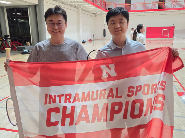 Intramural sports champions holding a red and white banner in an indoor gym.