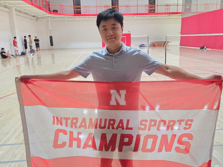 Person holding a red and white "Intramural Sports Champions" banner in a gymnasium.
