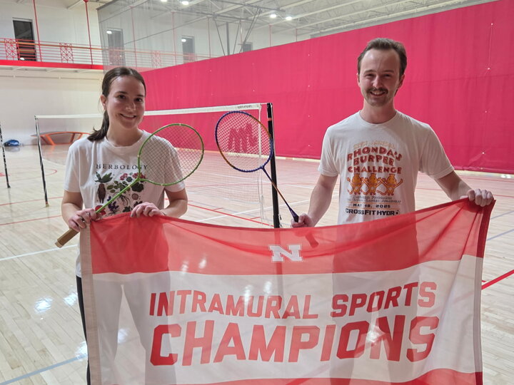 Two people holding a red banner reading "Intramural Sports Champions" in an indoor sports court.