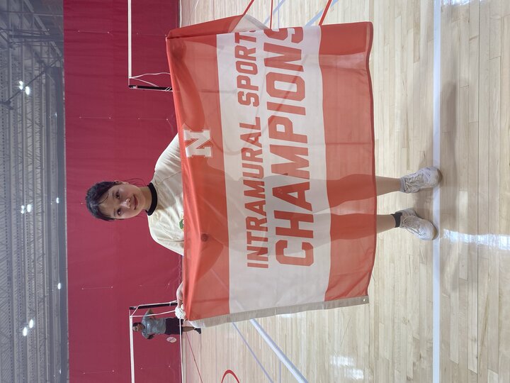 Person holding a red and white "Intramural Sports Champions" flag on a gym court.