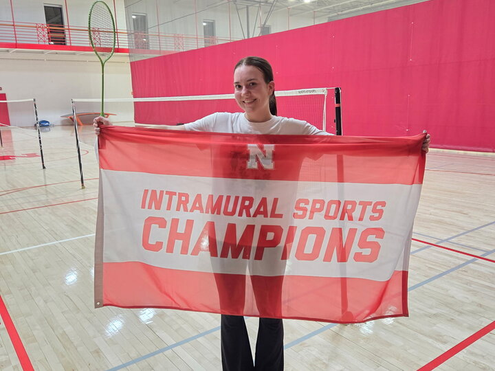 Person holding a red and white "Intramural Sports Champions" banner in a gymnasium.