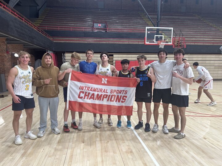 Group of young men holding a red banner on a basketball court indoors.