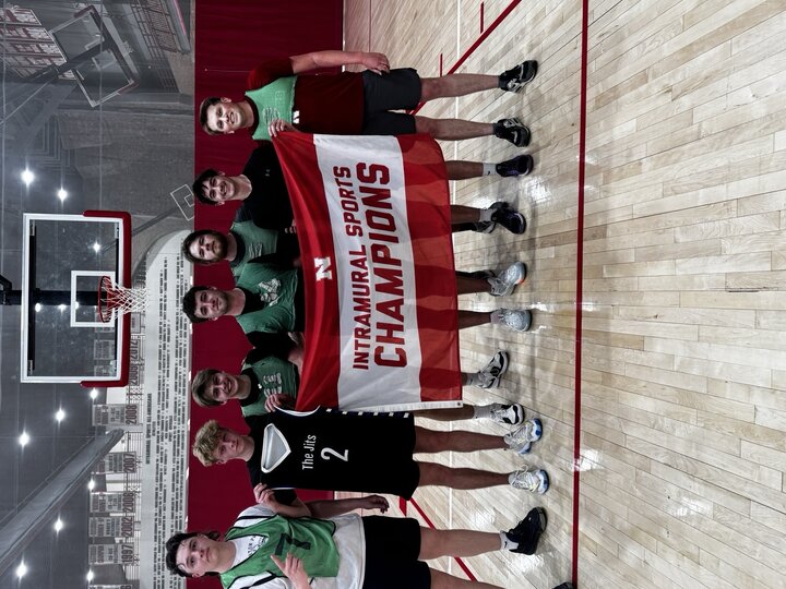 Group of smiling athletes holding a "Intramural Sports Champions" banner in an indoor basketball court.