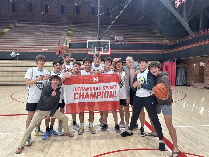 Team posing on basketball court with "Intramural Sport Champion" banner, smiling and celebratory.