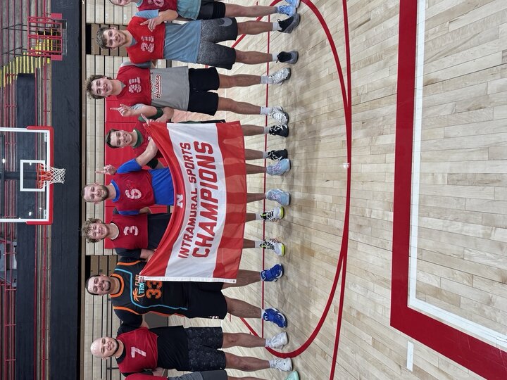 Team posing in a gym, holding a red and white "Intramural Sports Champions" banner.