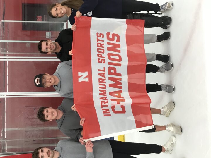 Five people on an ice rink holding a red and white "Intramural Sports Champions" banner.