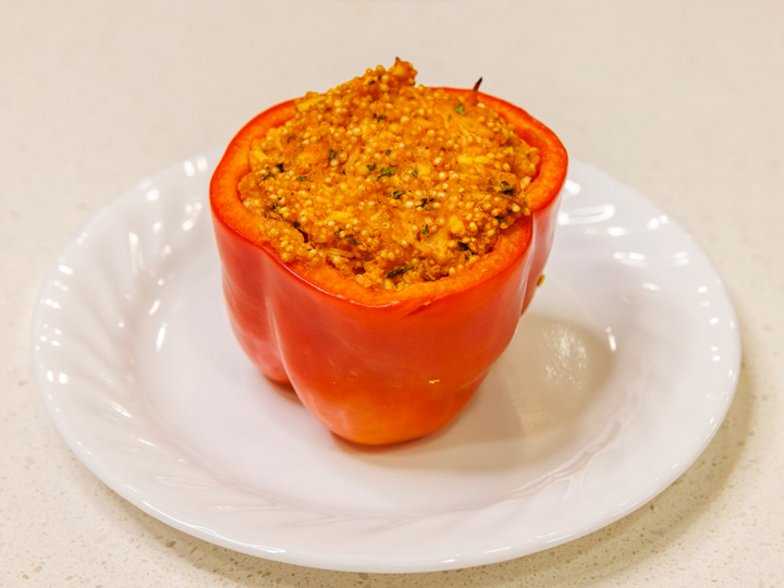 One red bell pepper sits on a white plate, stuffed with shredded buffalo chicken