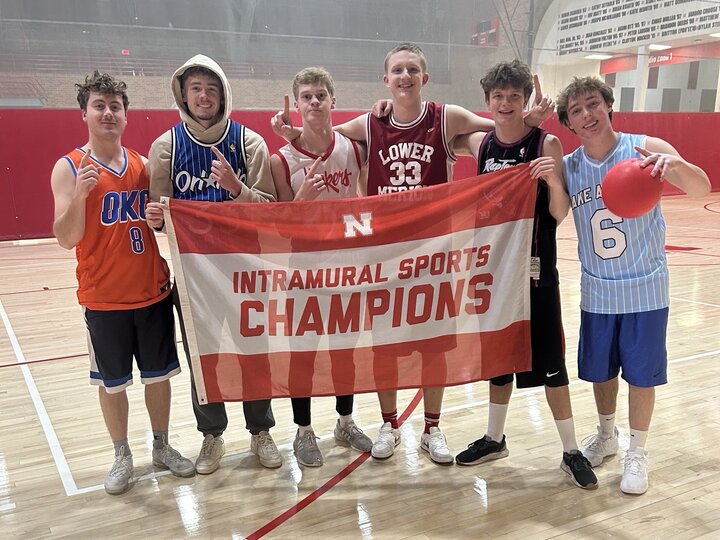 Group of basketball players holding a banner reading "Intramural Sports Champions" in a gym setting.