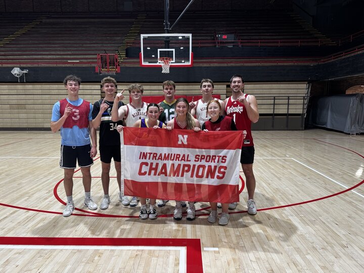 Intramural basketball team smiling on court, holding a red banner that reads "Intramural Sports Champions."