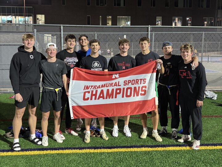 Group of students posing with flag on turf fields.