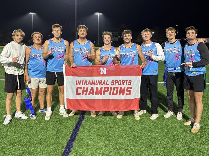 Group of students posing with flag on turf fields.
