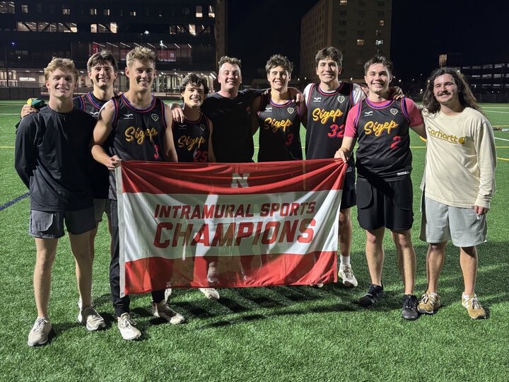 Group of students posing with flag on turf fields.