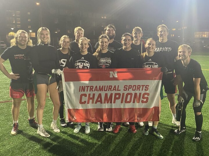 Group of students posing with flag on turf fields.