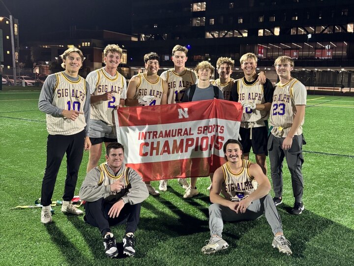 Group of students posing with flag on turf fields.