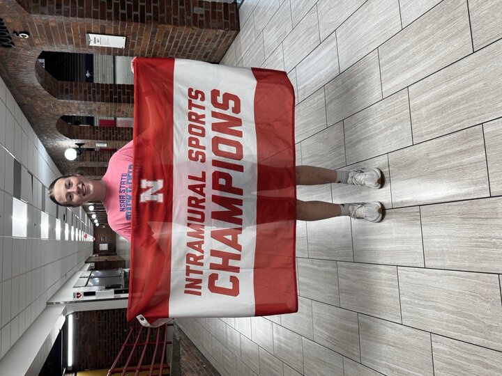 Person holding a red and white banner that reads "Intramural Sports Champions" in a hallway.