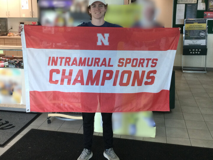 Red and white banner with "Intramural Sports Champions" held by a person in a lobby setting.