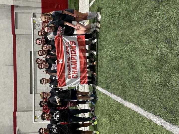 Group of people on an indoor soccer field holding a red banner reading "Intramural Sports Champions."