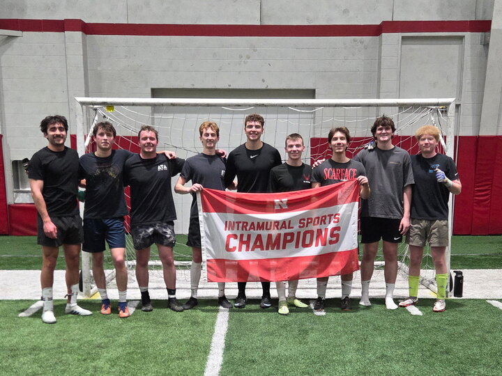 Team holding a "Intramural Sports Champions" banner in front of a soccer goal on indoor turf.