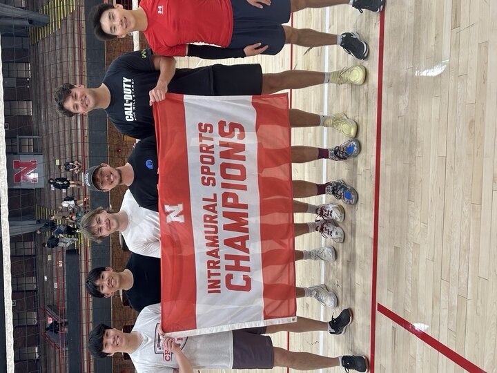 Seven men on a gym court holding a red and white "Intramural Sports Champions" banner.
