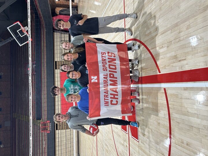 Group holding a "Intramural Sports Champions" banner on a volleyball court.