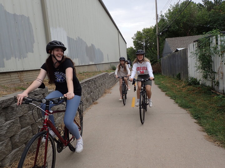 Three people riding bikes on a paved path, smiling and wearing helmets.