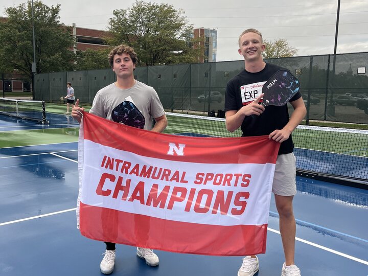 Two students posing with flag and pickleball paddles.