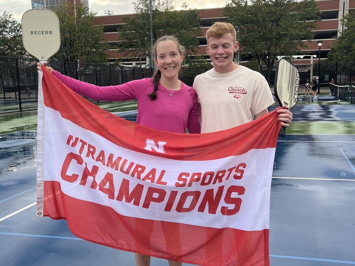 Two students posing with flag and pickleball paddles.