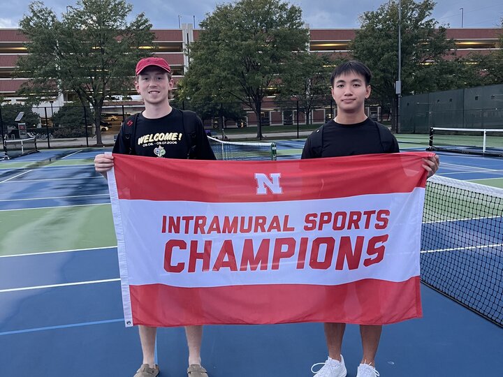 Two Students posing with flag and pickleball paddles.