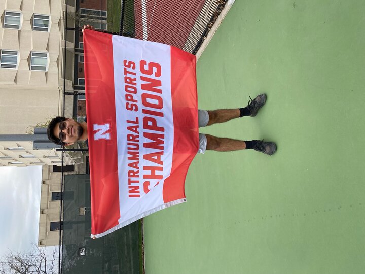 Man holding a red and white banner reading "Intramural Sports Champions" on a tennis court.