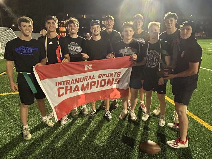 Group of students posing with flag on turf fields.